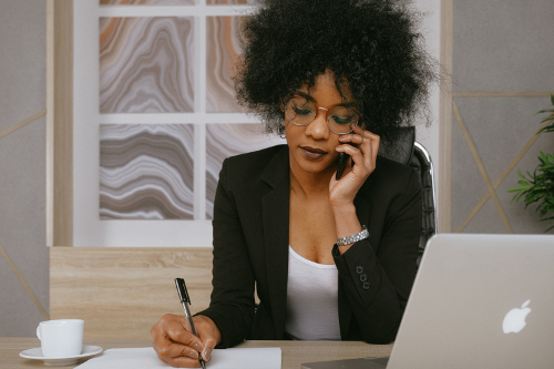 Black businesswoman on phone, writing on paper in office