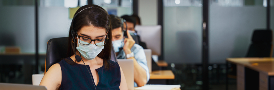 group of employees wearing protective masks and phone headsets in an office