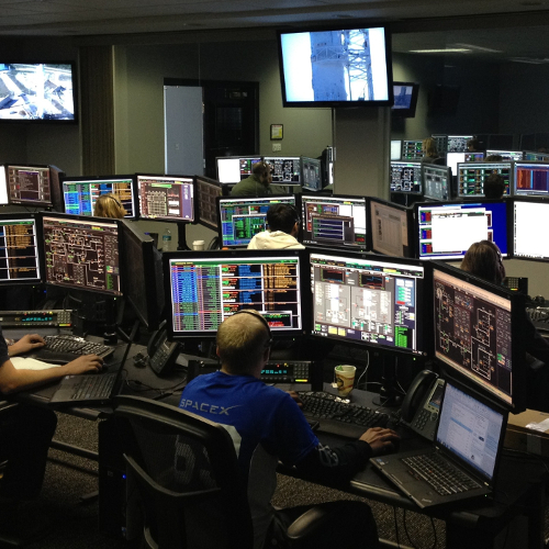 Internet technology specialists each working at stations with 3 monitors in a shared work environment.