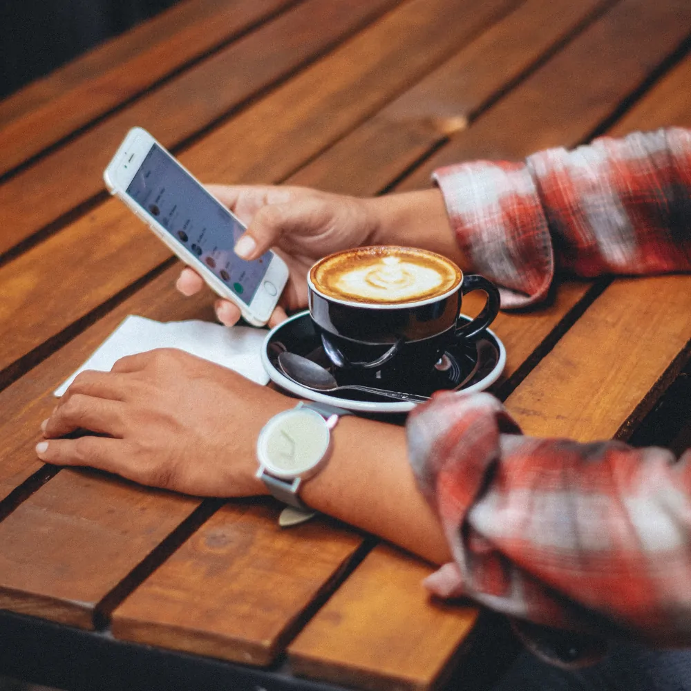 man's arms resting on table with latte between them and smartphone in right hand