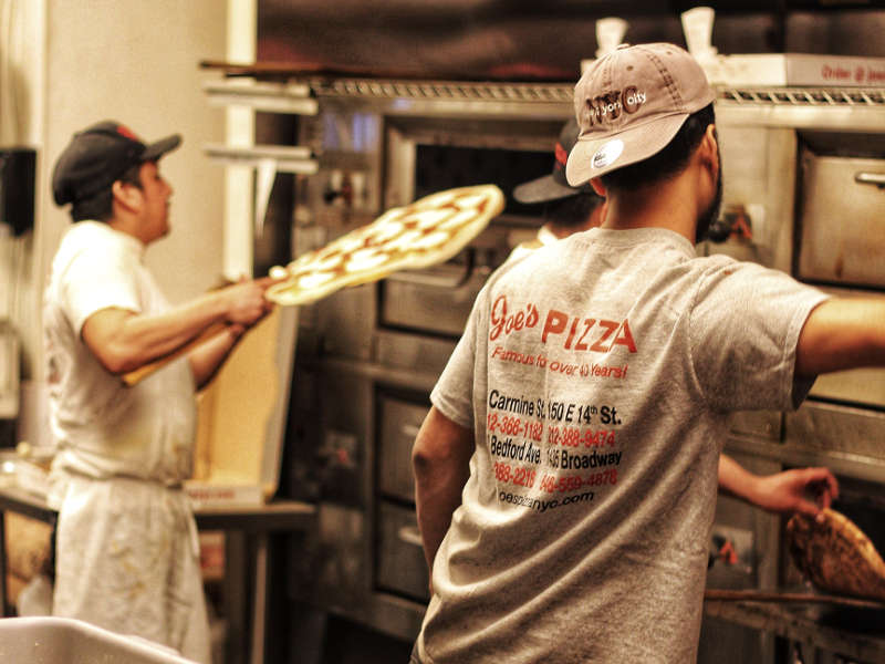 two pizza restaurant employees working in front of ovens