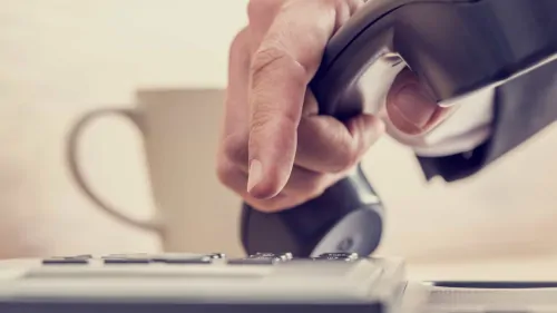 hand holding phone receiver with fingers dialing number with coffee cup in background