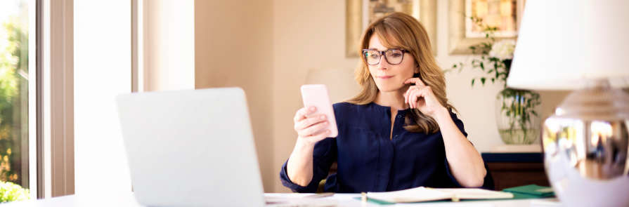 woman looks at smartphone while seated in home office