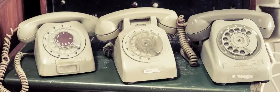 three older rotary phone in a row on a metal shelf