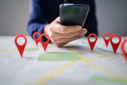 man holding phone with hand resting on map with location pins on it