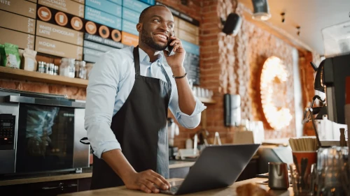 African-American businessman talking on phone while behind counter of coffee shop
