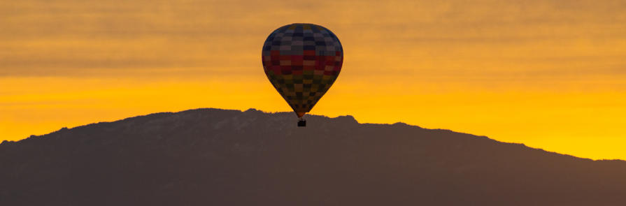 hot air balloon suspended in front of desert hill with sunrise in background