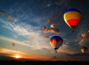 three hot air balloons flying with sunset in the background