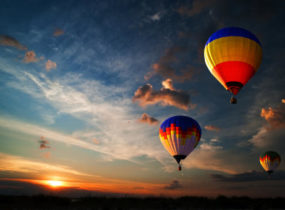 three hot air balloons flying with sunset in the background