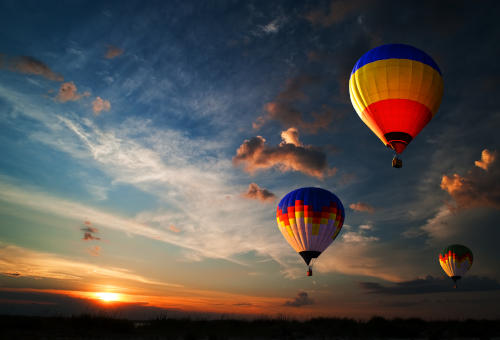 three hot air balloons flying with sunset in the background