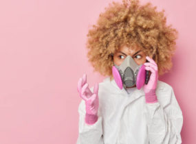 aggravated woman in respirator on cell phone against pink wall