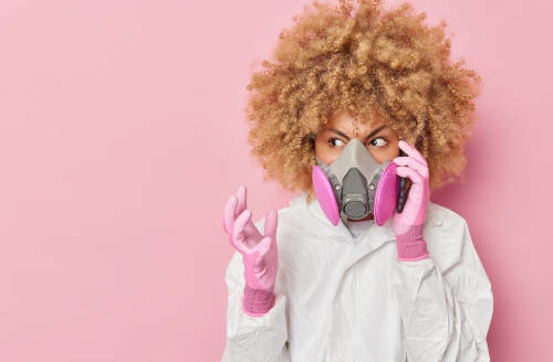 aggravated woman in respirator on cell phone against pink wall